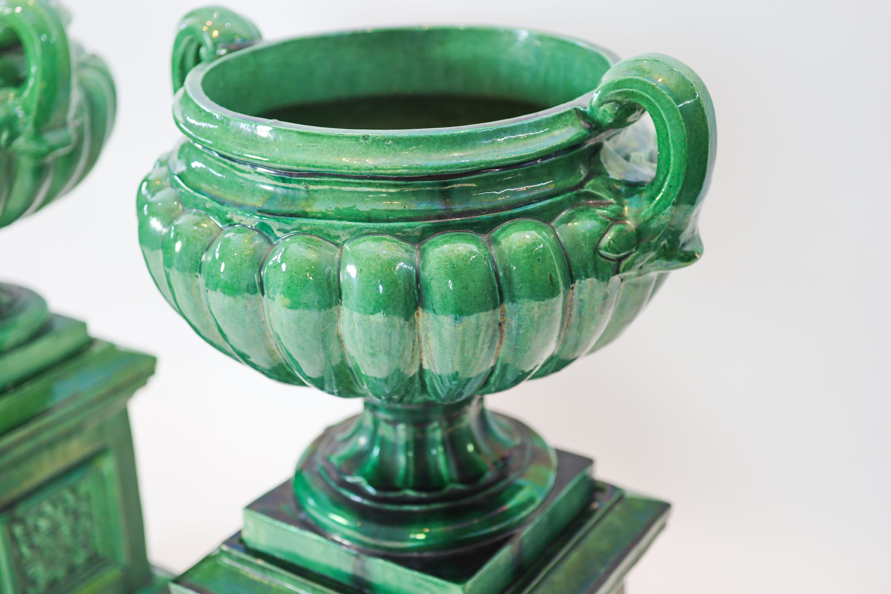 A pair of large dark green glazed terracotta fluted urns, raised on square plinths, diameter 50cm, height 101cm